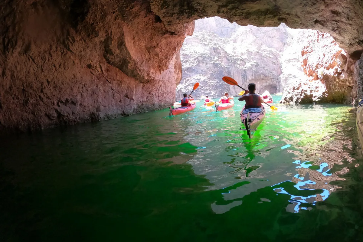 Group kayaking through cave with sunlight illuminating green water.
