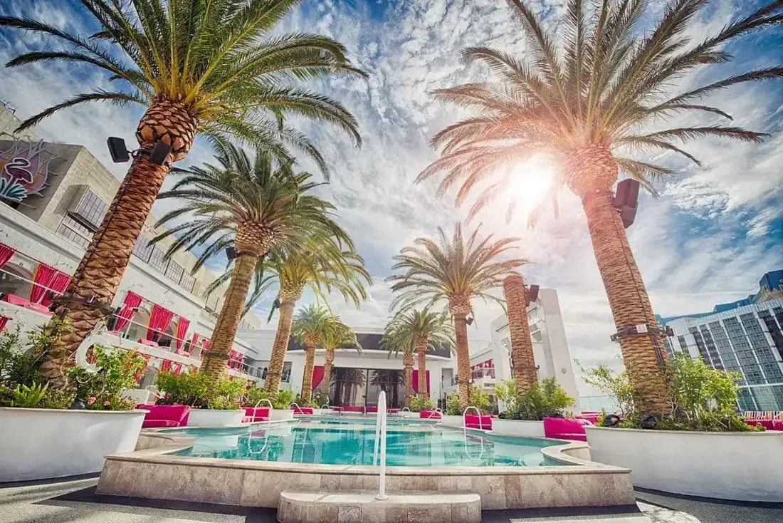 Tropical resort with palm trees, pool, and sunlit sky.