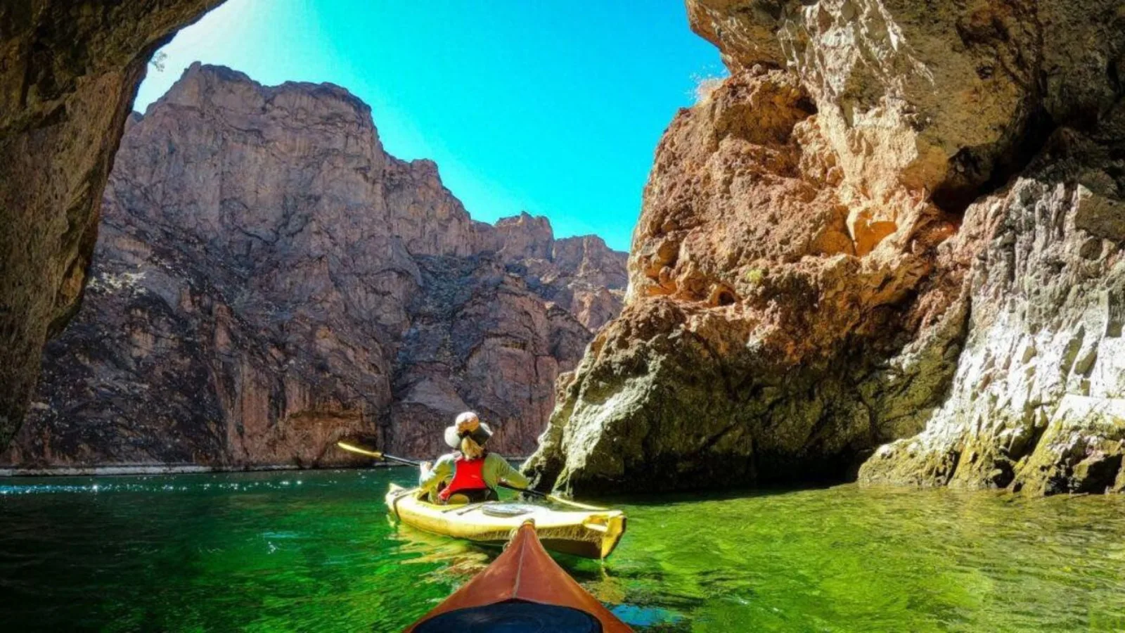 Kayaker paddling through the emerald water and steep cliffs of Black Canyon