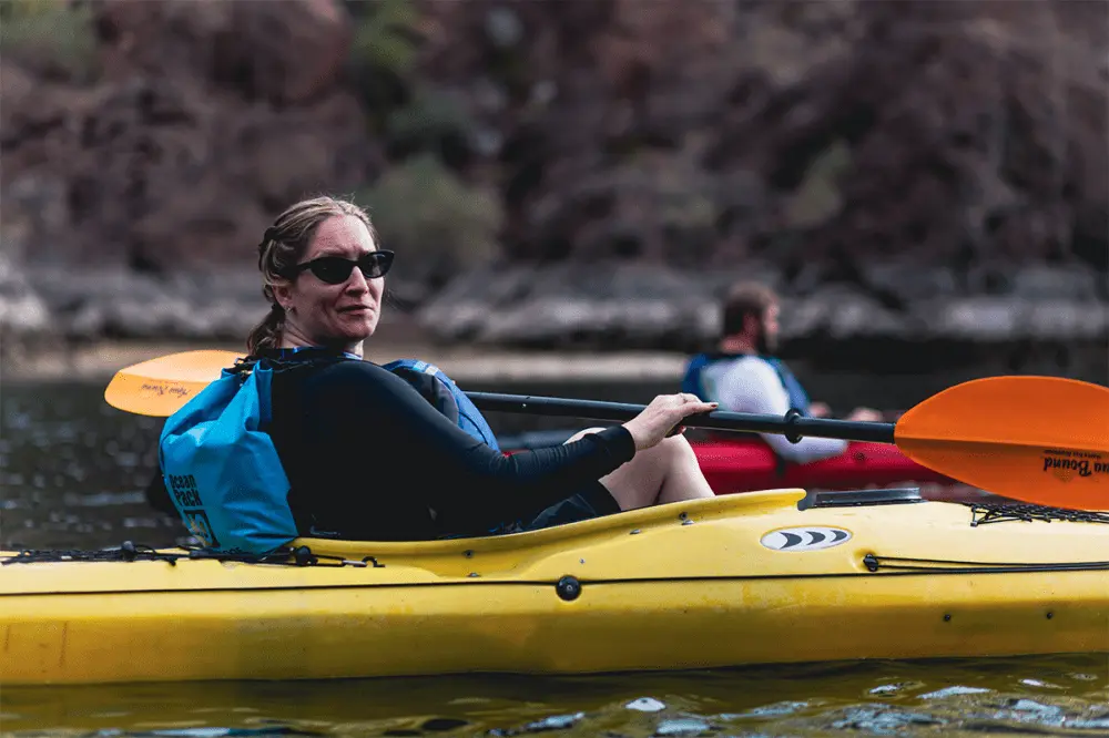 Woman in sunglasses kayaking on a river with another kayaker in the background