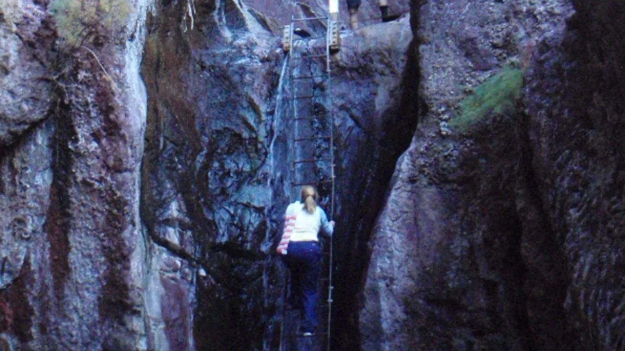 Person climbing a metal ladder in a rocky crevice