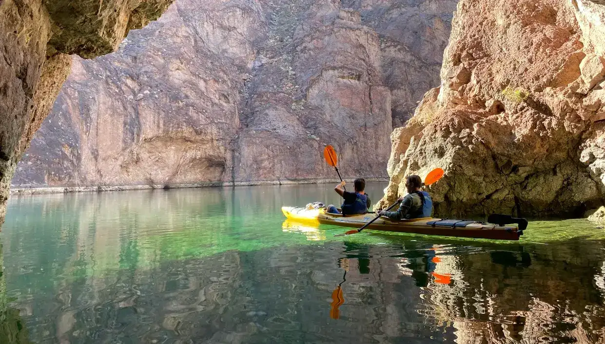 Two people kayaking on clear water through a rocky canyon.