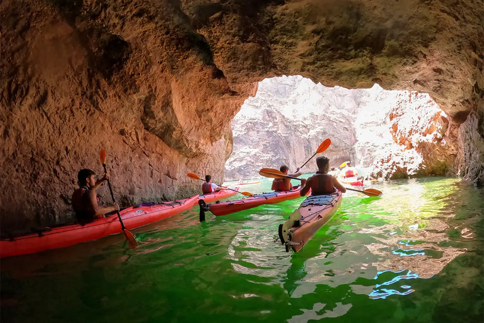 Kayakers in red kayaks paddling through Emerald Cave with sunlight at the entrance