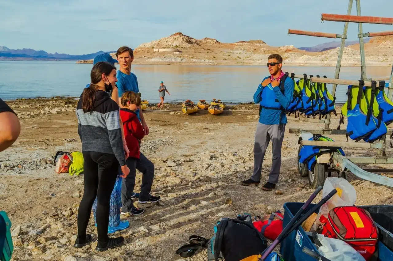 Group by lake with life jackets and kayaks, surrounded by rocky landscape.