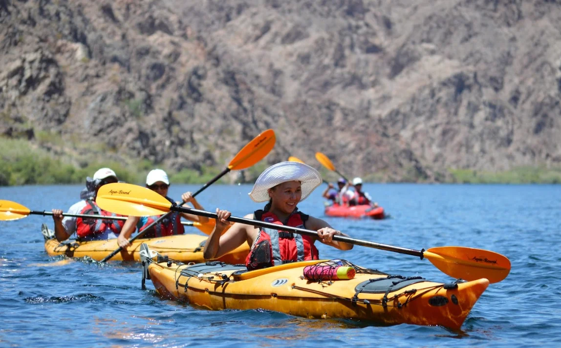 People kayaking on a lake with a rocky background.