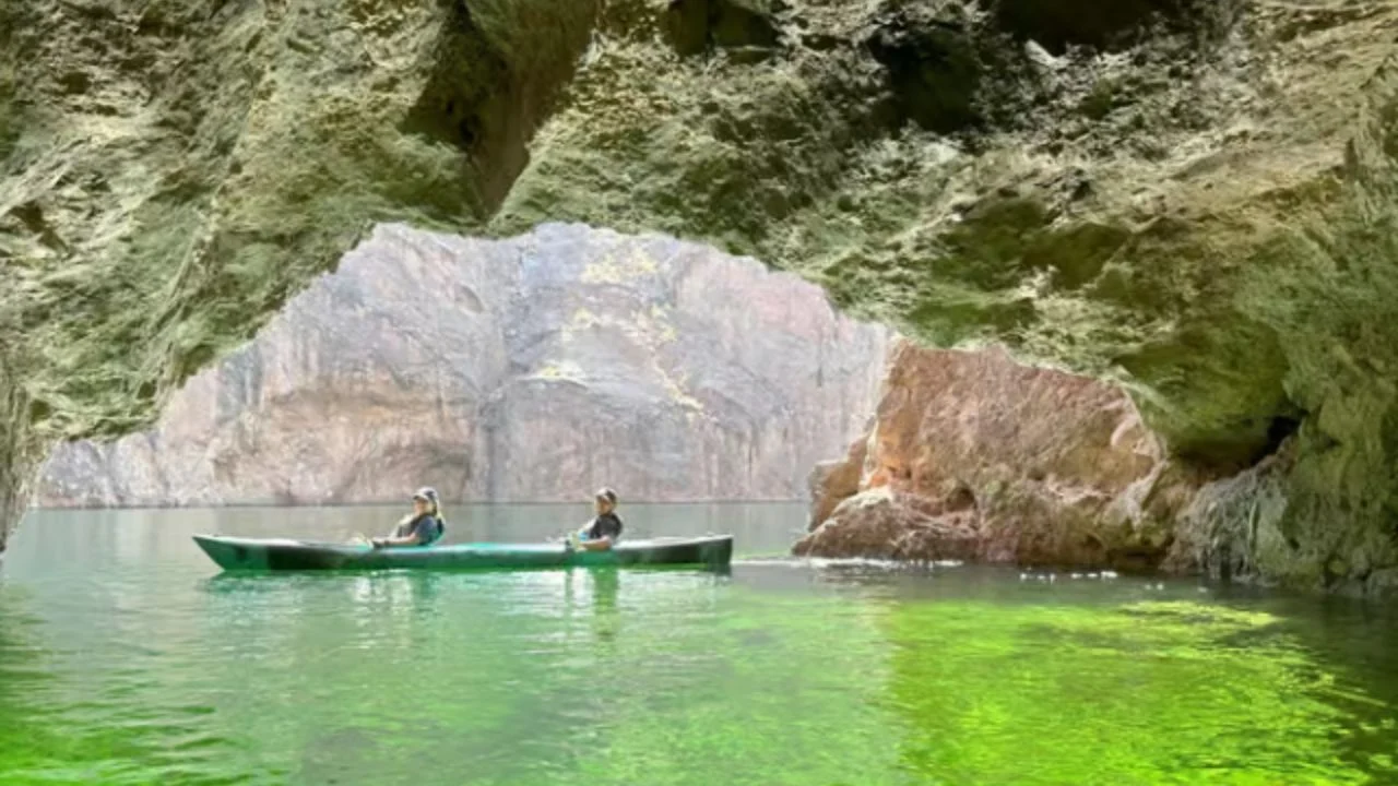 Kayakers inside Emerald Cave with bright green glowing water and canyon walls visible through the cave opening.