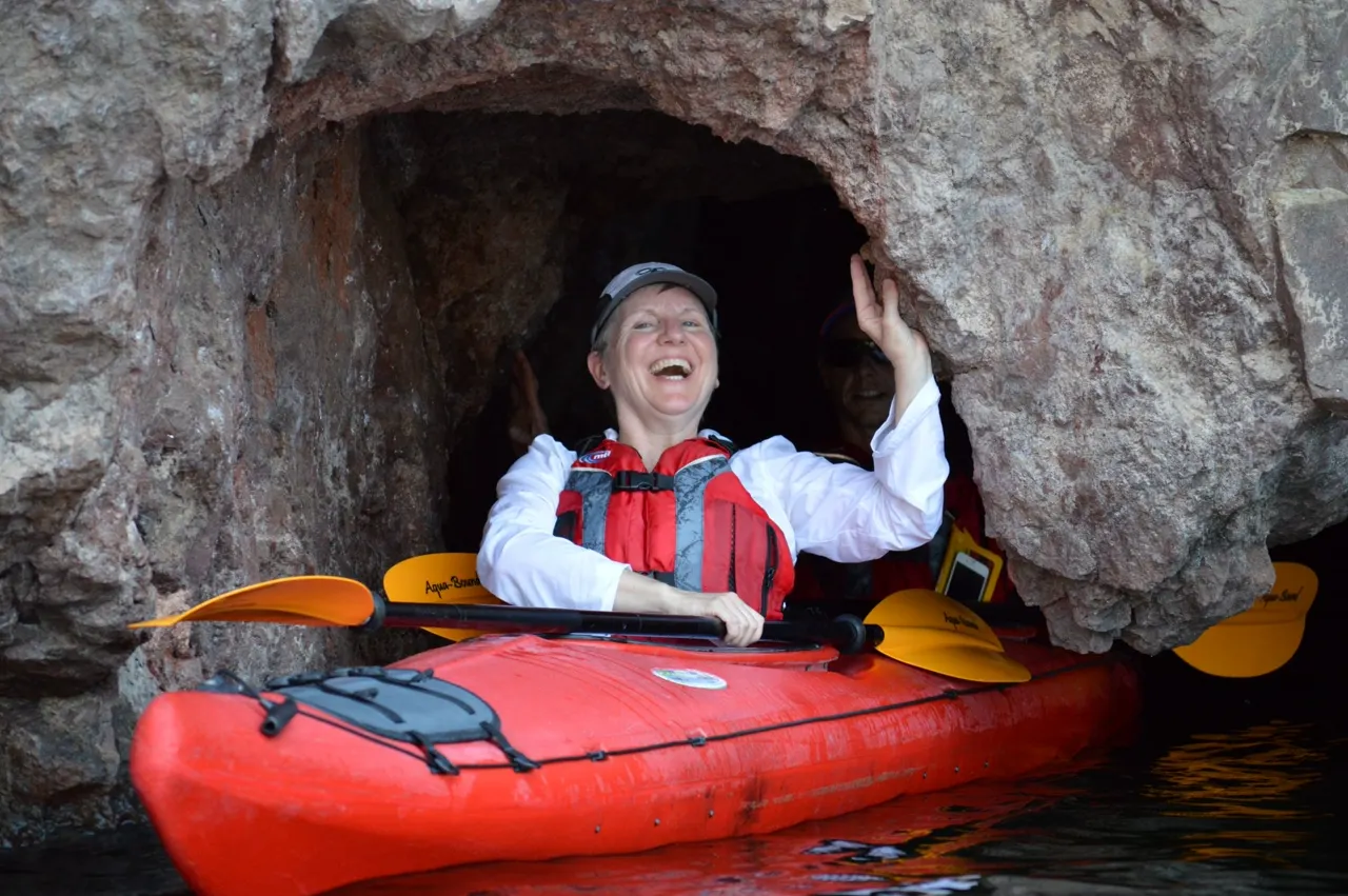 A smiling kayaker in a red touring kayak inside a rock alcove on the Colorado River near Las Vegas.