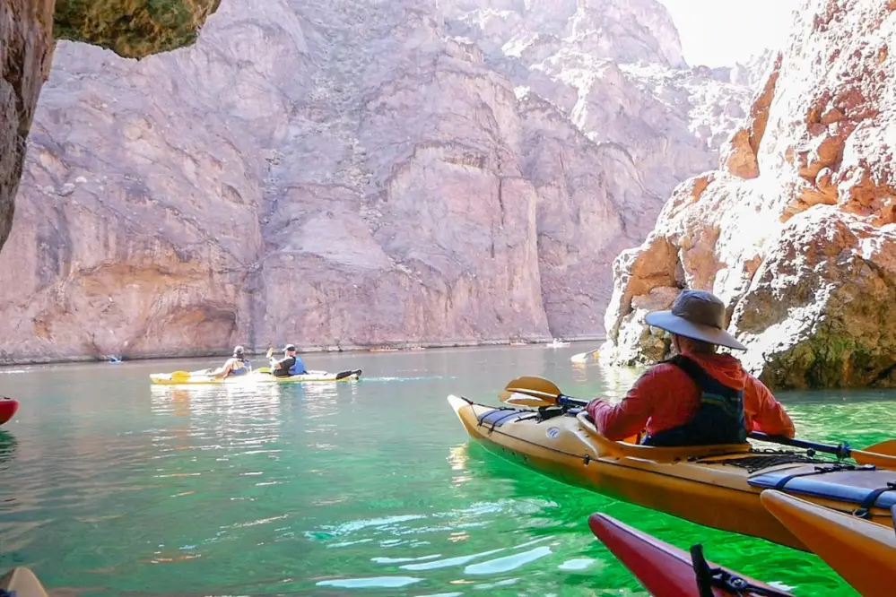 People kayaking on calm green water among rocky cliffs