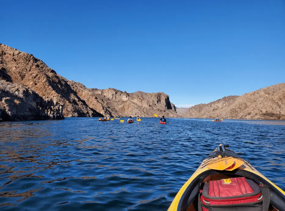 Kayakers paddling on a lake surrounded by rocky hills under a clear blue sky.