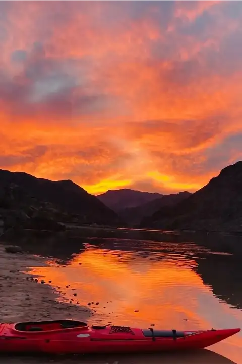 Fiery orange and pink sunset reflecting over the Colorado River with a kayak on shore