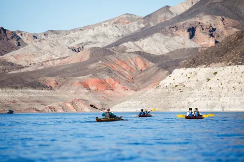 Kayakers paddling past striped desert hills on Lake Mead