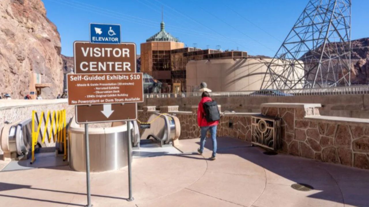 Woman in red jacket walks toward Hoover Dam Visitor Center sign