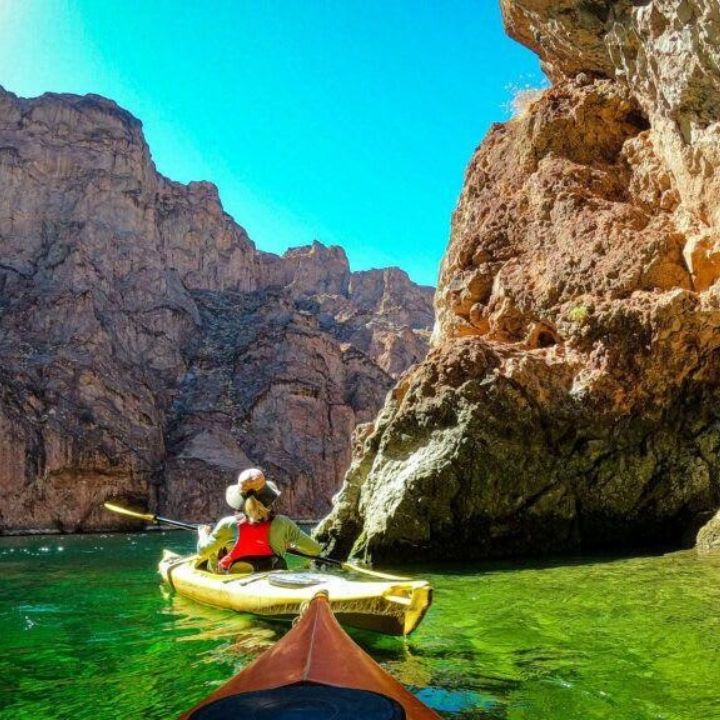 Woman kayaking through Black Canyon's emerald waters amid towering Nevada cliffs.