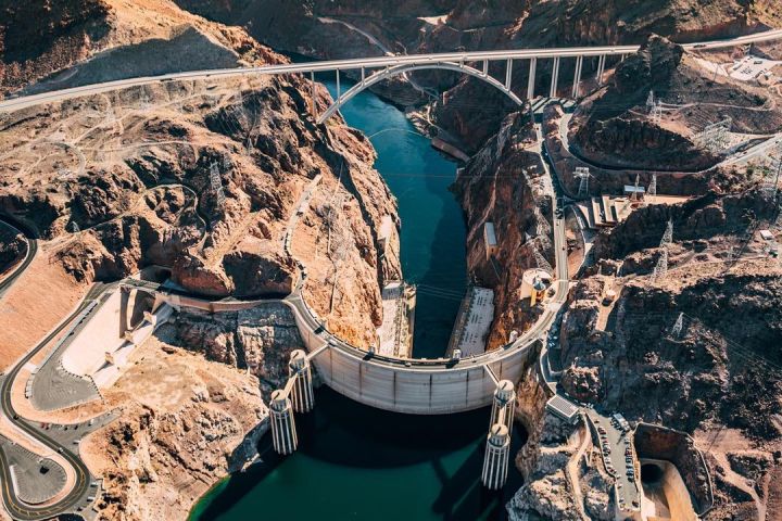 Aerial view of a dam with a bridge over a river between rocky mountains.
