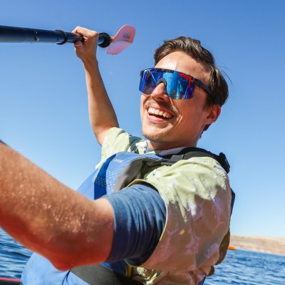 Man smiling in sunglasses, paddling a kayak on a sunny day.