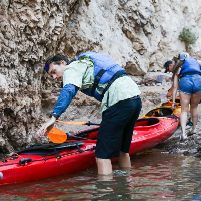 People with kayaks in a rocky canyon, wearing life vests and preparing to paddle.