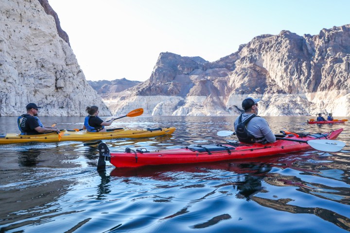 People kayaking on a calm lake with rocky cliffs in the background.