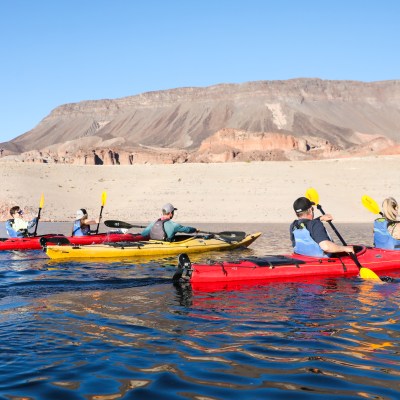 Group kayaking on a lake with rocky hills in the background.