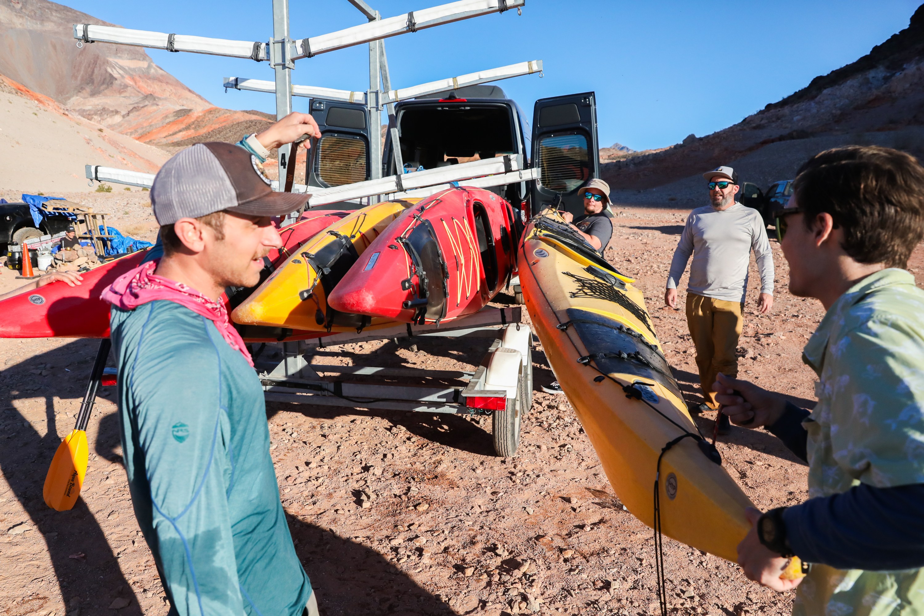Group of people loading kayaks onto a trailer in a rocky, desert landscape.