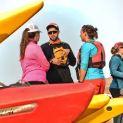 Group of people in outdoor gear talking beside kayaks.