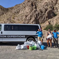 Group posing with collected trash bags by a van, in front of rocky hills.