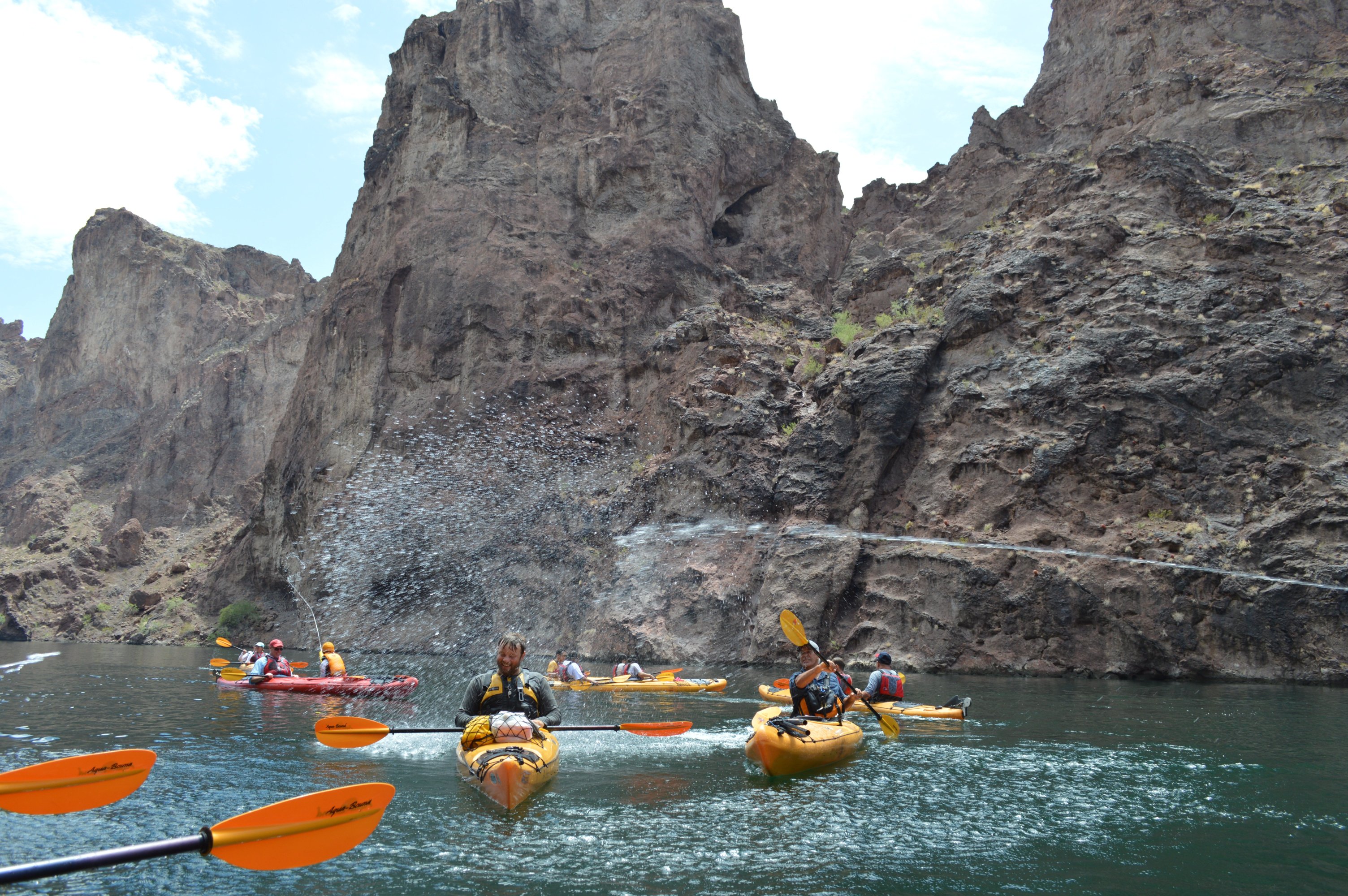 People kayaking in a canyon with water splashing around them.