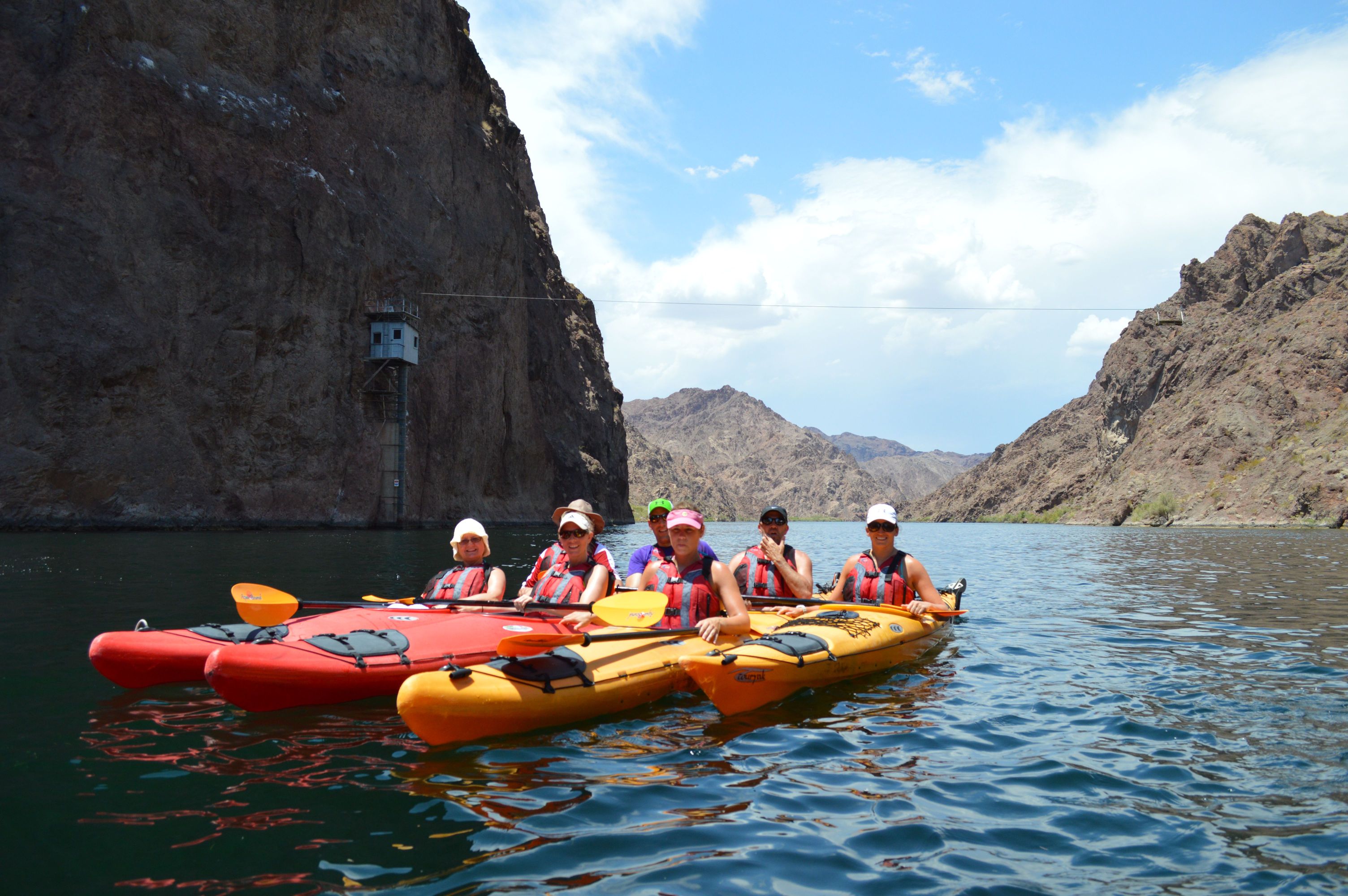 Group kayaking on a calm river between rocky cliffs.