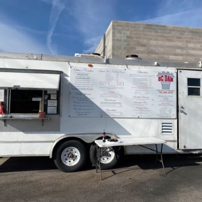 White food truck with menu displayed, serving window open, blue sky background.