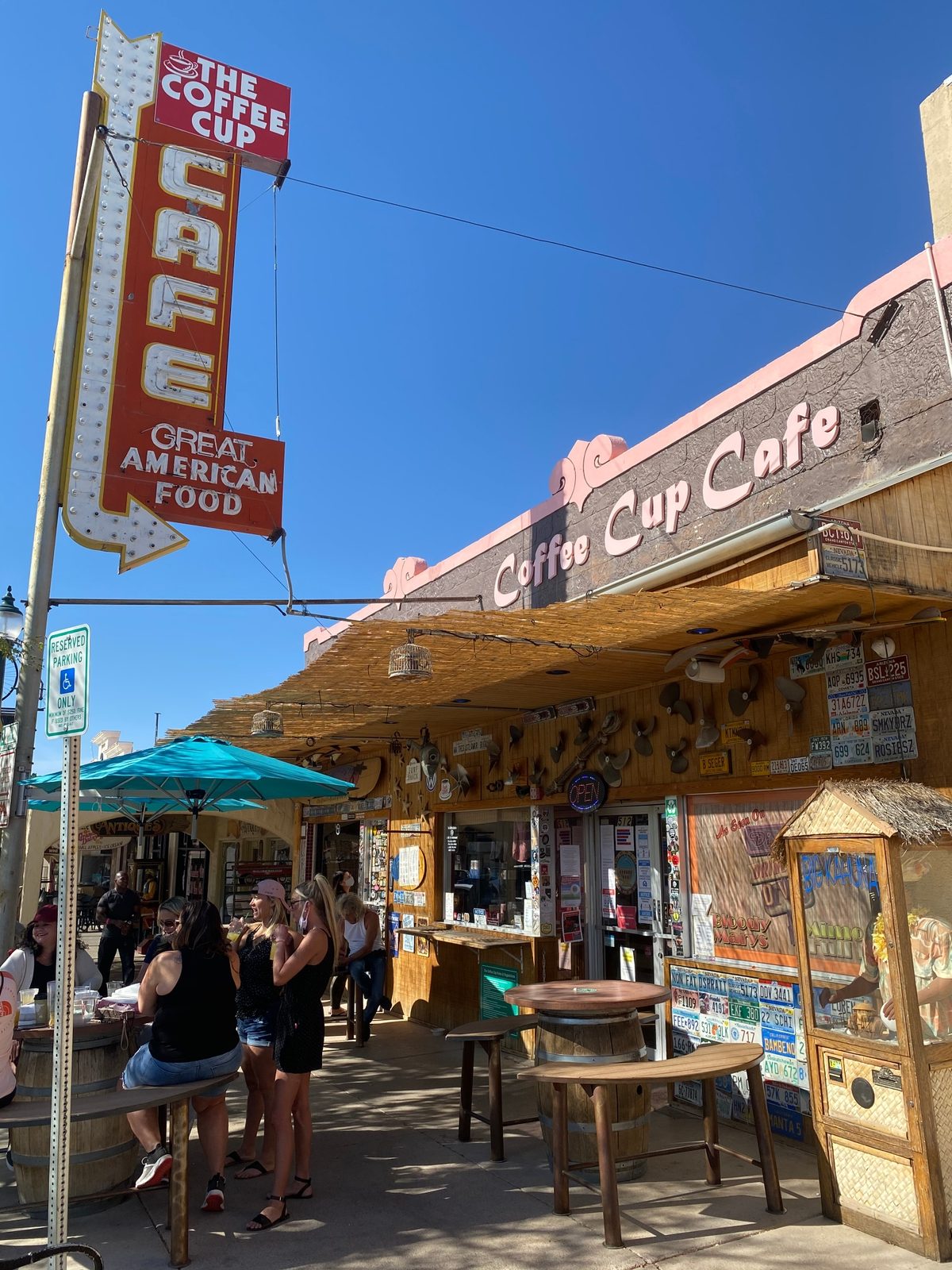 Outdoor cafe with vintage neon signs and patrons enjoying a sunny day.