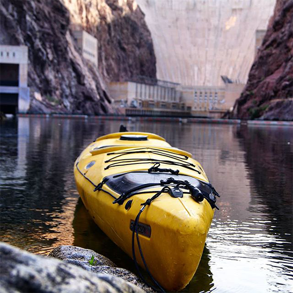 Yellow kayak on water near a large dam and rocky cliffs.