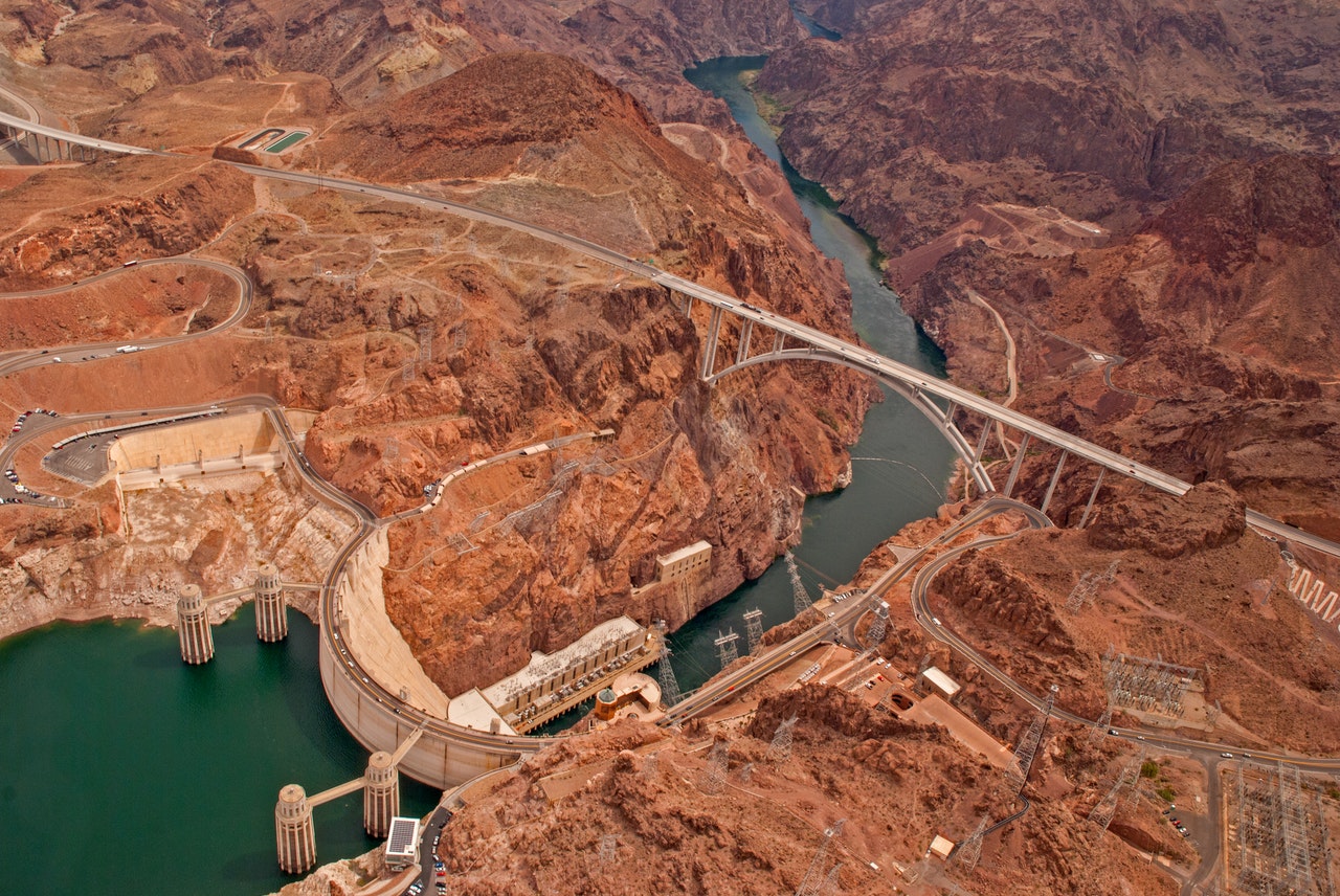 Aerial view of a large dam and bridge crossing a canyon with a river below.