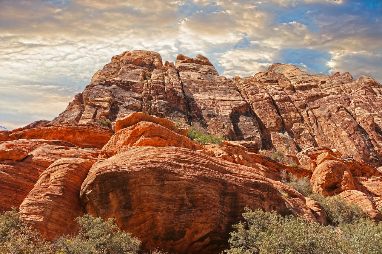 Red rock formations under a partly cloudy sky with lush greenery at the base.