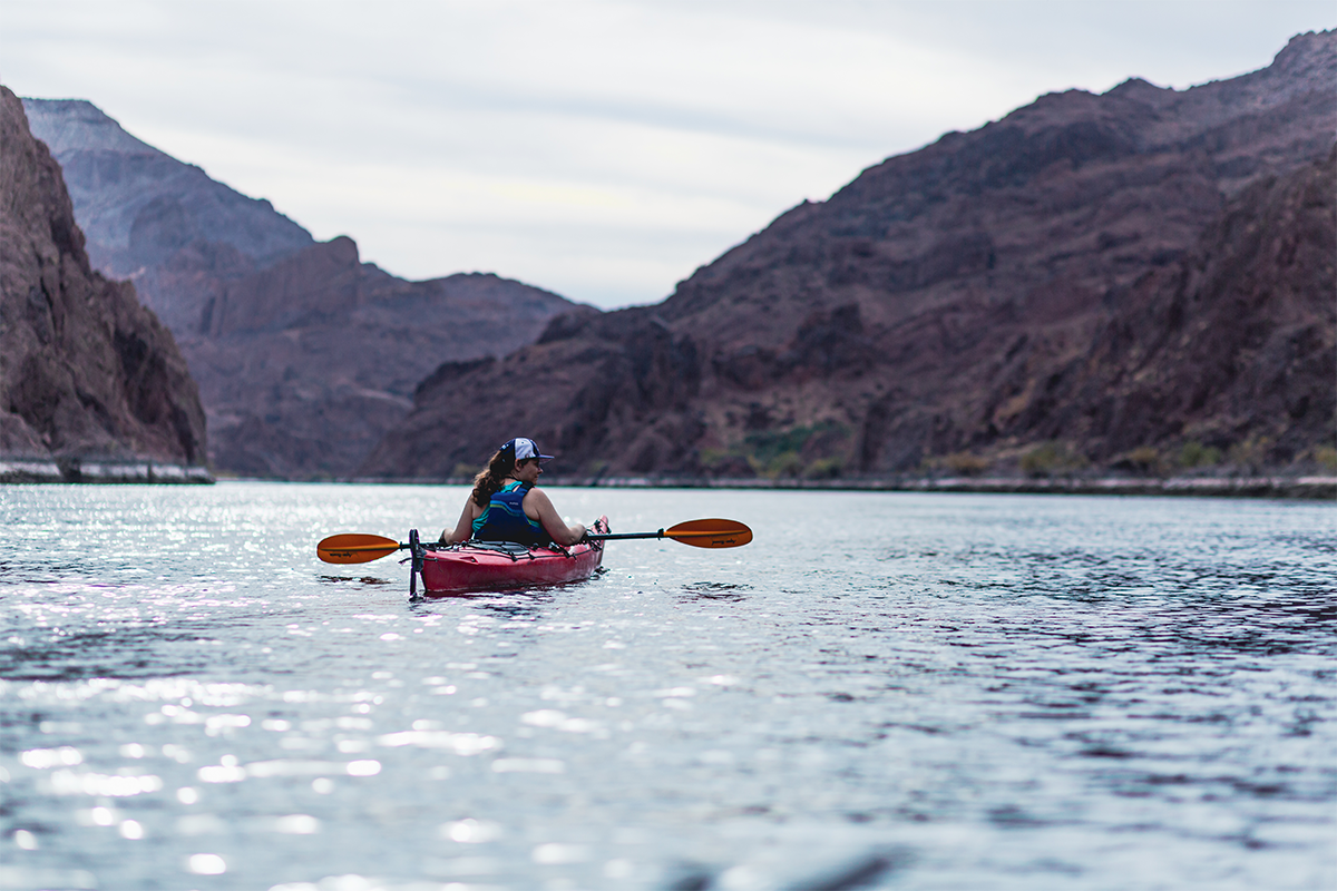 Person kayaking on a river surrounded by rocky mountains.