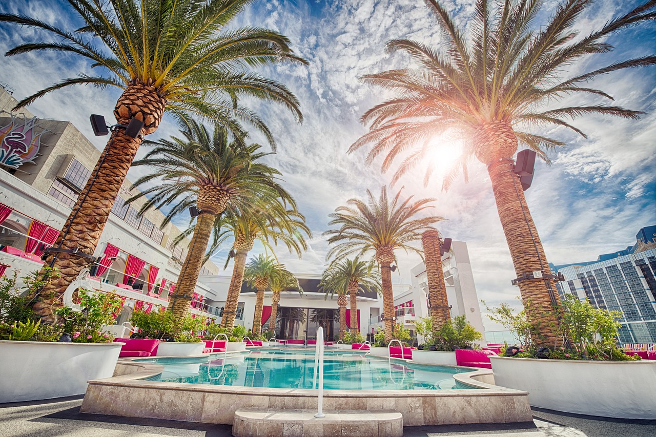 Tropical resort with palm trees, pool, and sunlit sky.