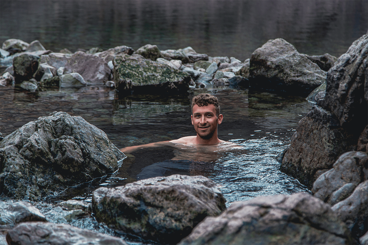 Person smiling while partially submerged in a rocky outdoor pool.
