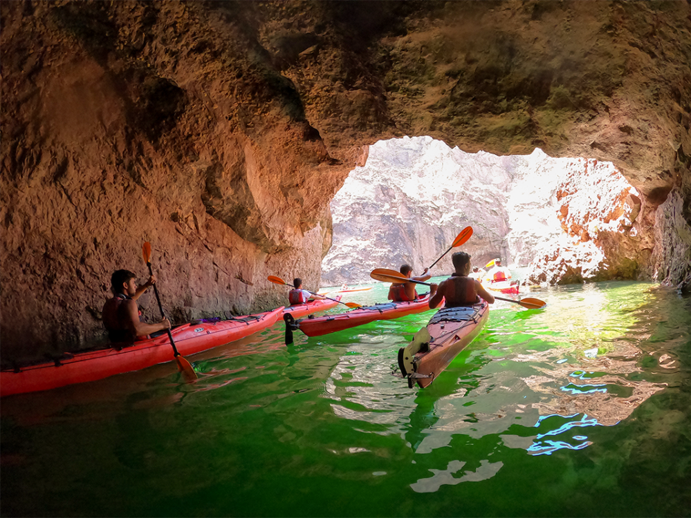 People kayaking in a cave with sunlight illuminating the entrance.