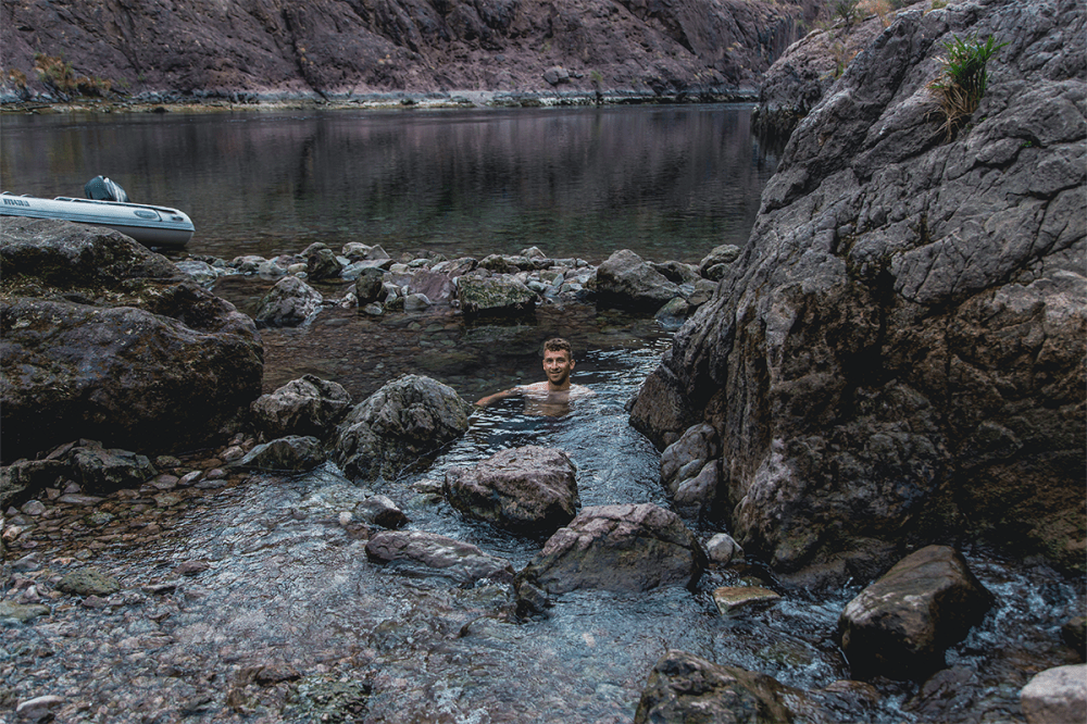 Person swimming in a rocky river with inflatable boat nearby.