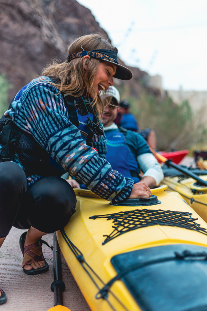 Woman smiling while adjusting a yellow kayak with a group in outdoor setting.
