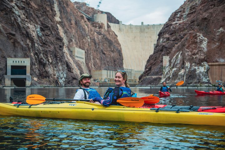 People kayaking near a dam with rocky cliffs in the background.