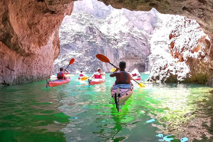 Group of kayakers paddling through a rocky cave with green water.
