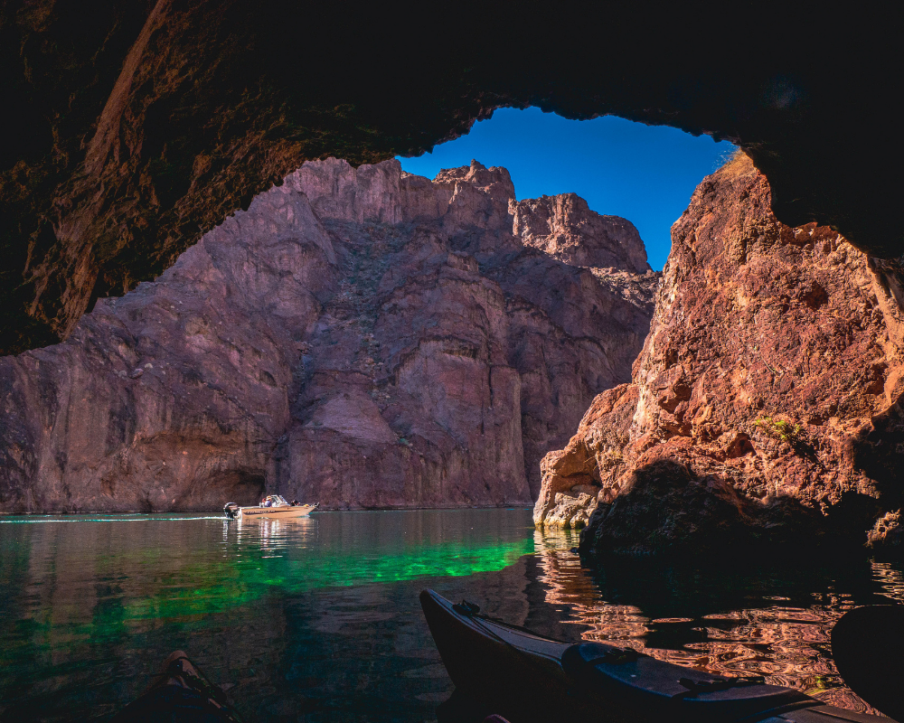 Cave entrance view with boat on green water and rocky cliffs under blue sky.