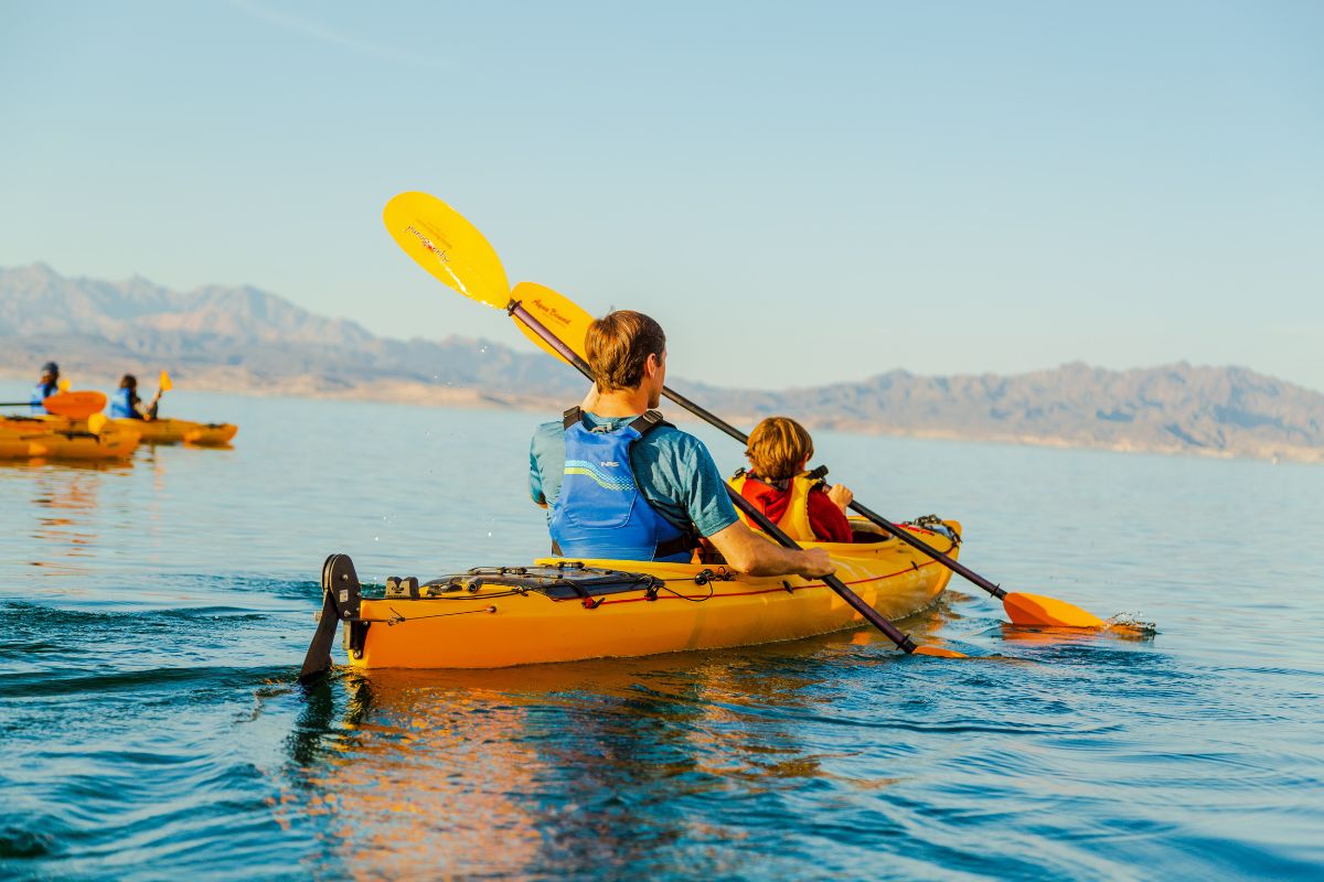 People kayaking on calm water with mountains in the background.