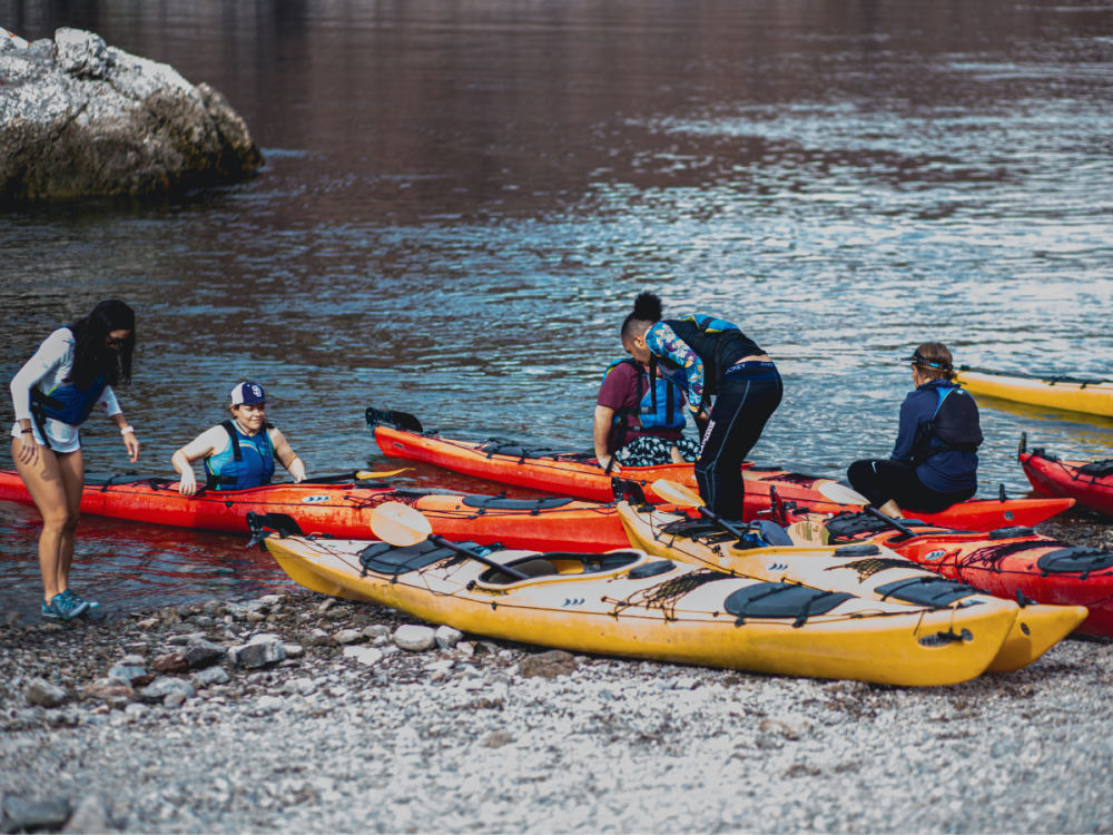 Group of people preparing kayaks on a rocky shore by the water.