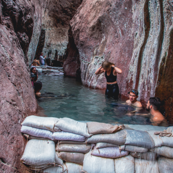People enjoying a natural hot spring surrounded by rocky cliffs.
