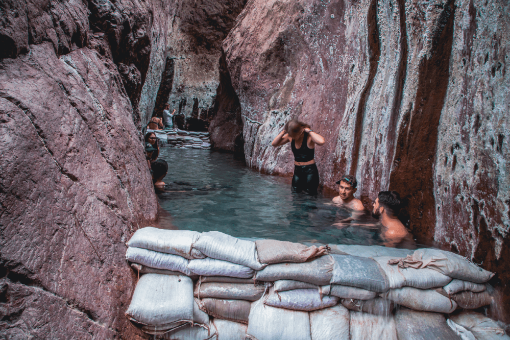People enjoying a natural hot spring surrounded by rocky cliffs.