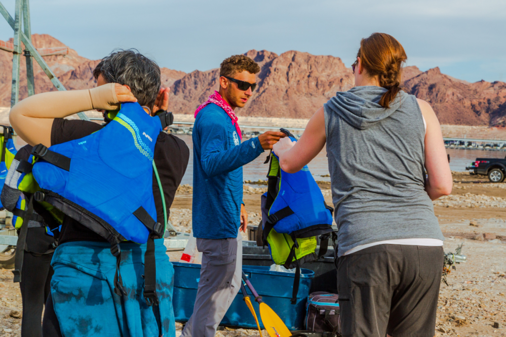 Group of people with life jackets near rocky landscape and water.