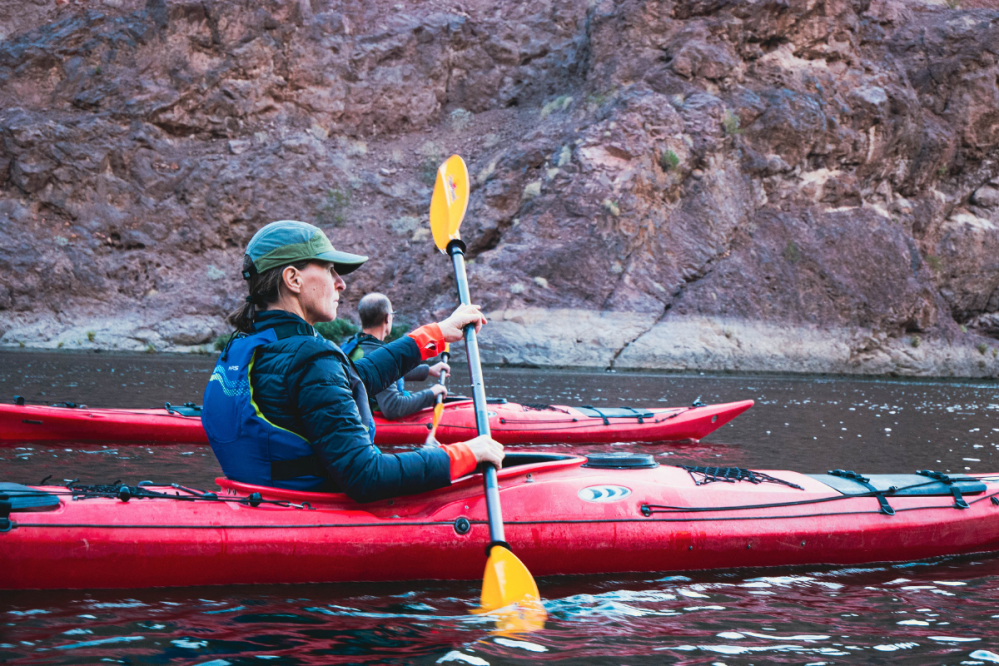 People kayaking on a river near rocky cliffs.