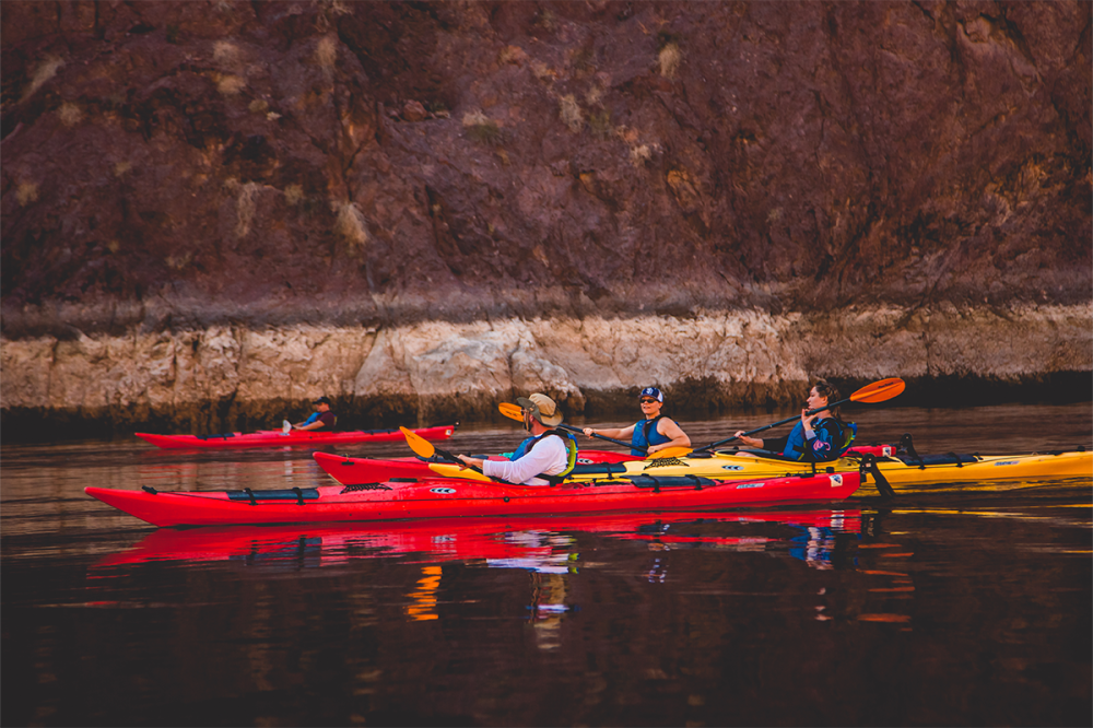 Group kayaking on calm water near rocky cliffs, with vibrant red and yellow kayaks.