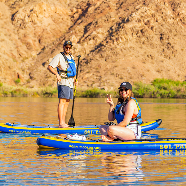 Two people paddleboarding on a calm river, with rocky hills in the background.