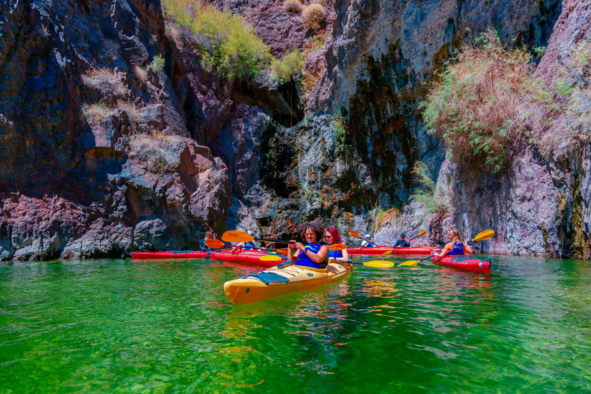 Group kayaking on bright green water near rocky cliffs with vegetation.